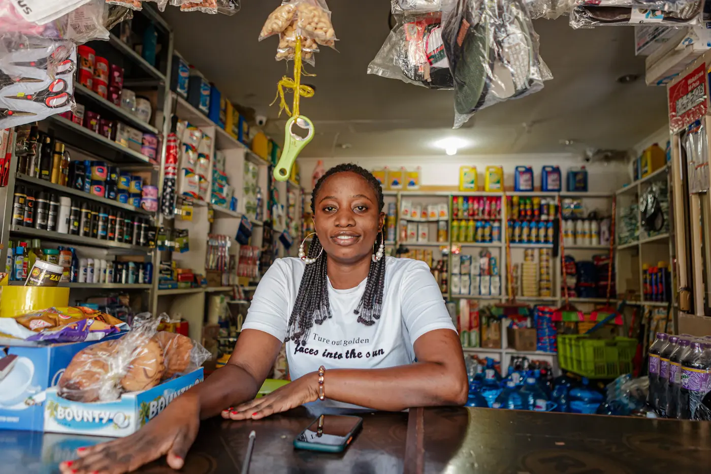 A shop owner leaning on her counter in a small, well-stocked store