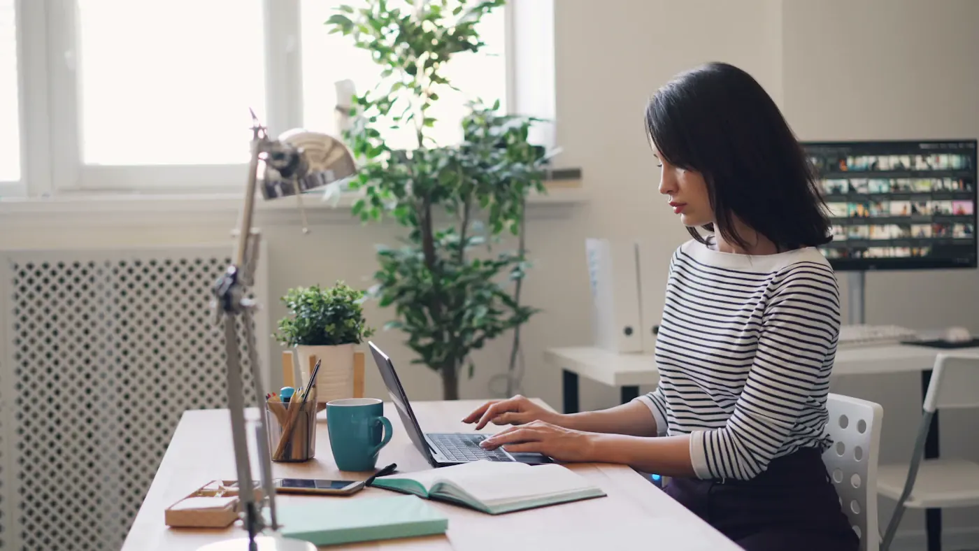 A woman working at a laptop at a desk by a window